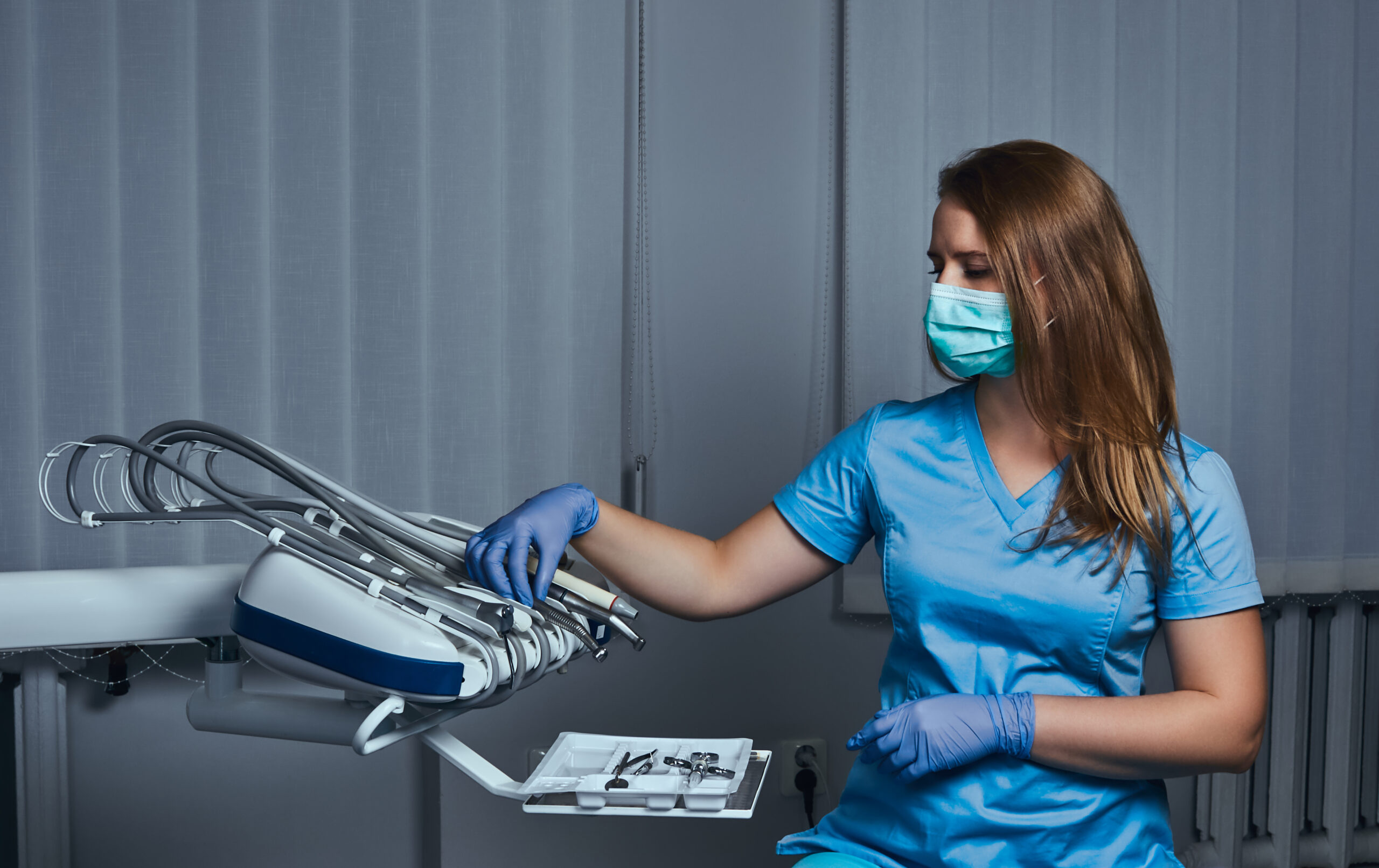 Female dentist wearing a uniform and mask sitting on a chair at his workplace in a dental clinic.