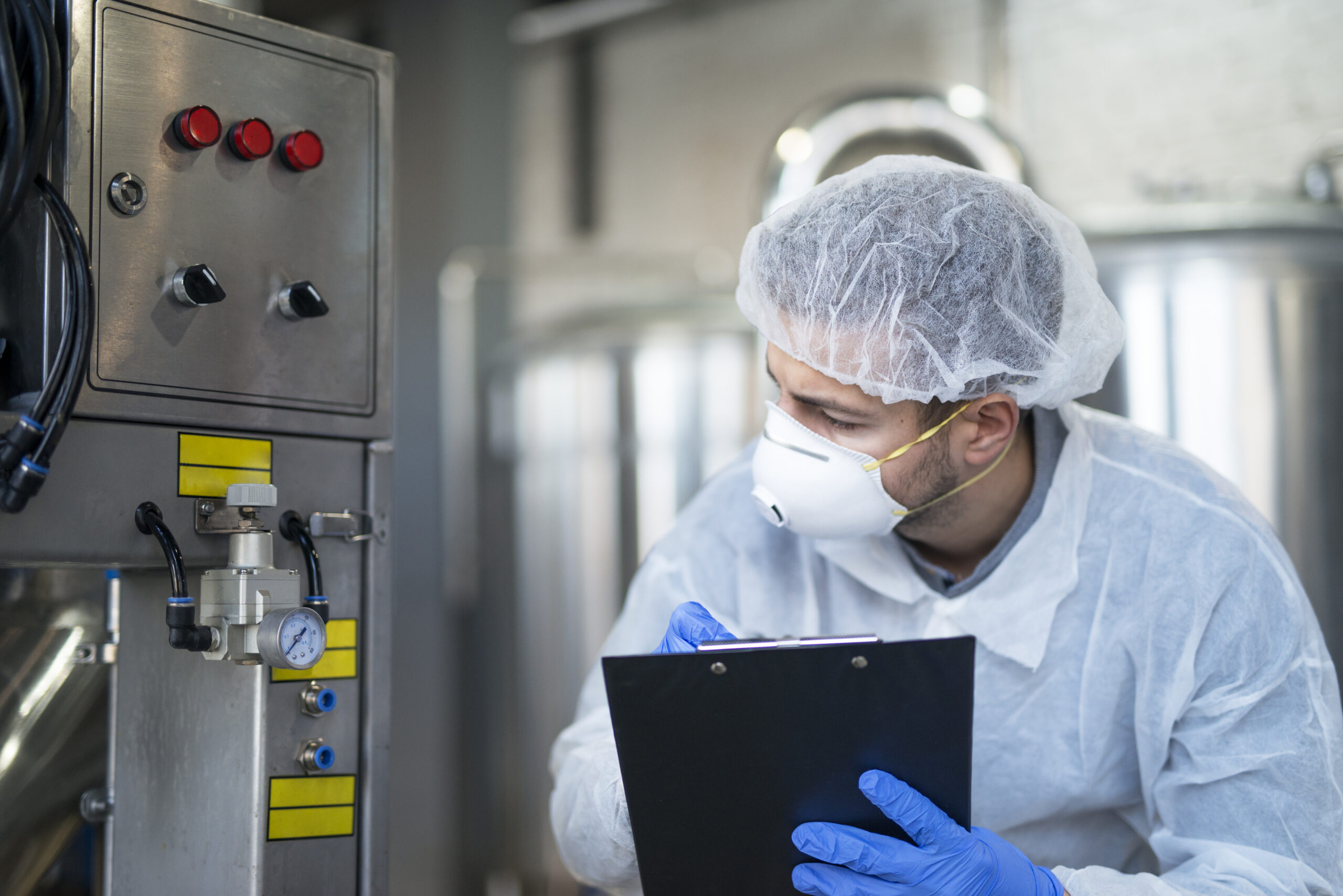 Young technologist in white protective uniform controlling industrial machine at production plant.